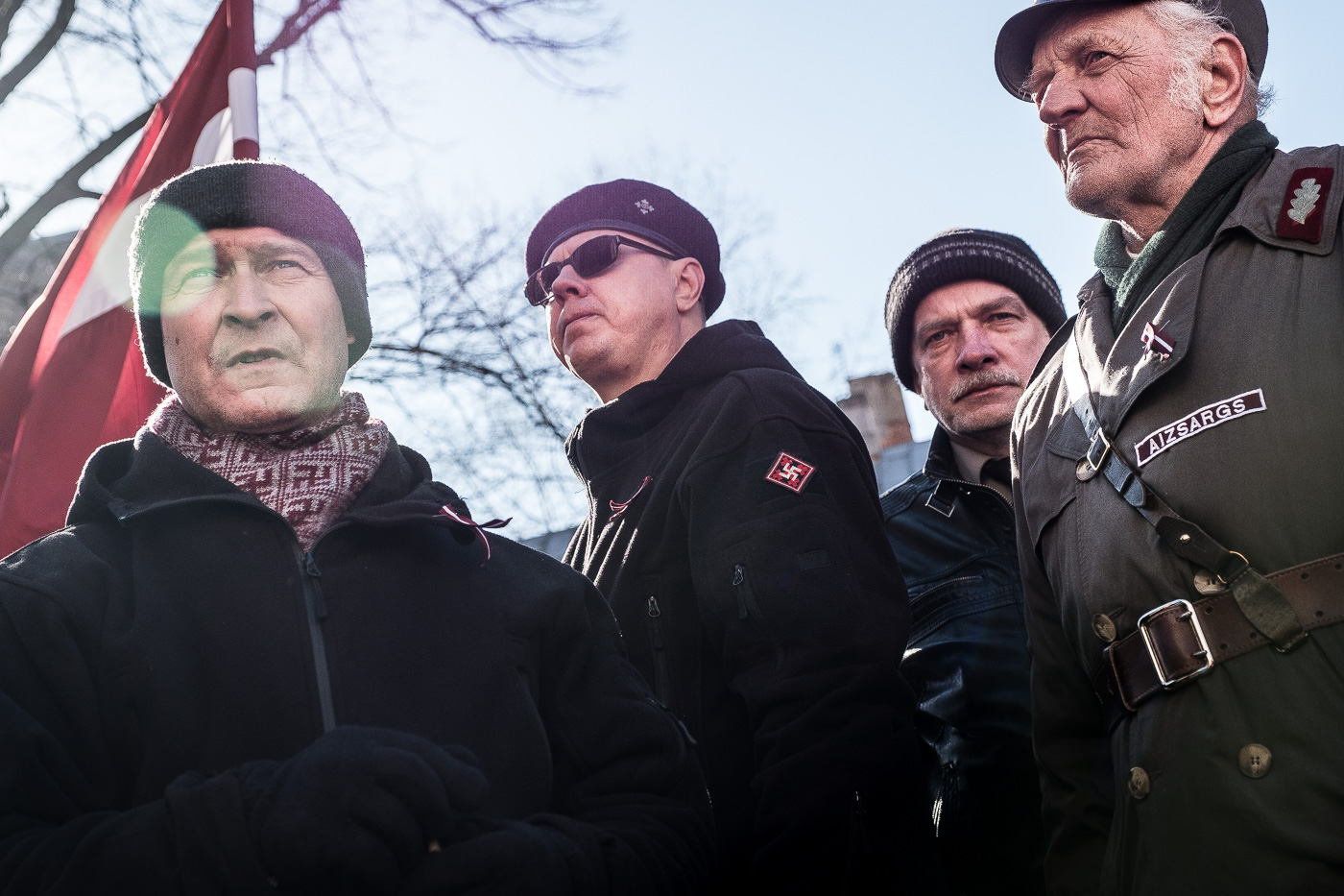 Activistes amb l’emblema del Pērkonkrusts acompanyant un veterà de la Legió Letona. A l’esquerra, amb la bufanda feta de sauvàstiques, Igors Šiškins, condemnat a dos anys de presó per participar en un atemptat amb bomba